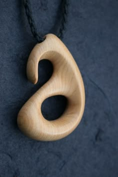 a wooden pendant is hanging from a black cord on a dark surface, with the letter s carved into it