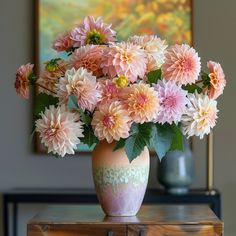 a vase filled with pink and white flowers on top of a wooden table next to a painting