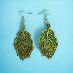 pair of earrings with green and gold leaf design on blue background, close up view