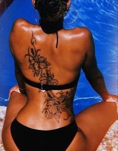 a woman sitting in front of a swimming pool with tattoos on her back