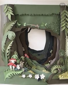 an open cardboard box with paper cut outs and flowers on the inside, along with plants and mushrooms