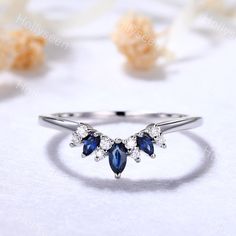 a white gold ring with blue and clear stones on it, sitting next to some flowers