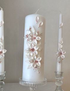 three white candles with flowers on them sitting next to each other