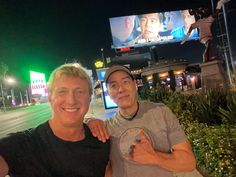 two men posing for a photo in front of a movie theater