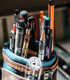 an assortment of pens and pencils in a wooden container