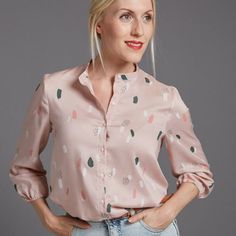 a woman with blonde hair wearing a pink shirt and blue jeans, standing in front of a gray background