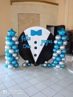 a man in a tuxedo with blue and silver balloons on the floor next to an arch