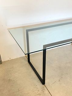 a glass table sitting on top of a cement floor next to a white wall with a black metal frame