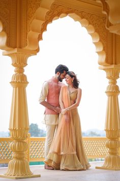 a man and woman standing in front of an archway with yellow pillars on either side