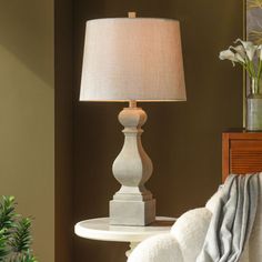 a white table lamp sitting on top of a wooden night stand next to a bed