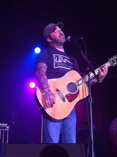 a man holding a guitar while standing in front of a microphone