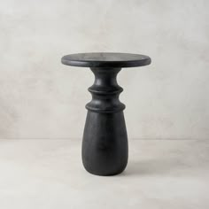 a small black table sitting on top of a white floor next to a gray wall