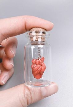 a person holding a tiny heart in a glass bottle with a chain attached to it