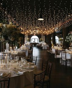 a banquet hall with tables and chairs covered in white tablecloths, lit by fairy lights