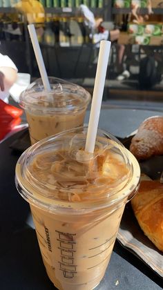 two plastic cups filled with liquid sitting on top of a table next to croissants