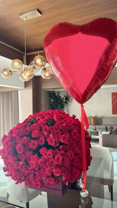 a heart shaped balloon sitting on top of a table next to a bouquet of red roses