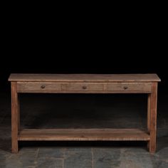 a wooden table sitting on top of a stone floor next to a black wall in the dark