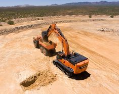 an orange excavator digging dirt in the desert