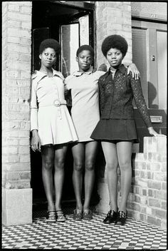 three women standing next to each other in front of a brick building