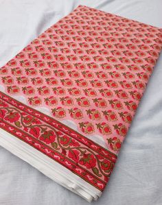 a pink and red cloth on top of a white bed sheet with an intricate design