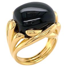 The striking opacity of black onyx is the summit of this ring. A cushion cabochon of the gem is further underlined by polished 18k yellow gold. Fluted tips of the metal overlap to surround the gem and descend into a multi-split shank. The total weight of the black onyx is 18 carats. Measurements for the ring are 0.88 inches (width) by 0.73 inches (length) by 1.14 inches (depth). Elegant Black Dome Ring With Polished Finish, Formal Black Dome Ring With Polished Finish, Modern Yellow Gold Dome Ring With Cabochon, Modern Cabochon Dome Ring For Formal Occasions, Modern Cabochon Dome Ring For Formal Events, Modern Dome Ring With Oval Cabochon For Formal Events, Black Cabochon Signet Ring For Formal Occasions, Elegant Black Oval Dome Ring, Modern Black Cabochon Rings