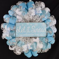 a blue and white mesh wreath with let it snow written on the front, surrounded by bows