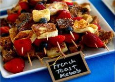 french toast kebabs with berries and blueberries on a white plate next to a sign