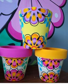 three colorful flower pots sitting on top of a wooden table next to a large painting