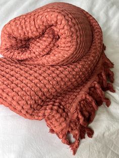 an orange knitted blanket laying on top of a white bed spread with tassels