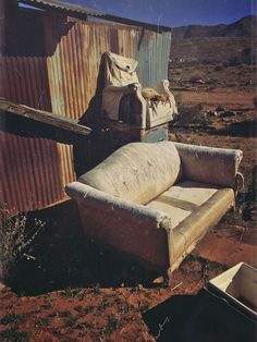 an old couch sitting in front of a rusty building with a bag on it's back