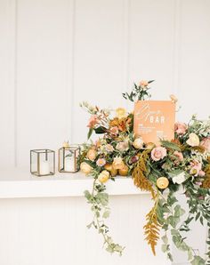 an arrangement of flowers and greenery on a mantel by a white painted wall