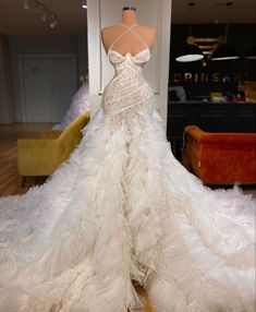 a white wedding dress on display in a room with couches and tables behind it