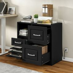 a black cabinet with drawers in front of a white wall and wooden floor next to a computer desk