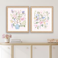 two framed paintings on the wall above a dresser with flowers and plants in vases