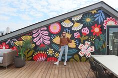 a woman standing on top of a wooden deck next to a wall covered in flowers