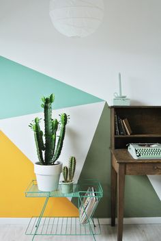 a desk with a keyboard and cactus in front of a wall painted with geometric shapes