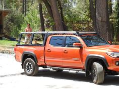 an orange truck parked in front of some trees and a man standing on top of it