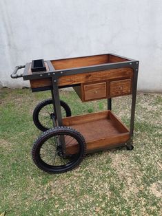 a wooden cart with wheels and drawers on the grass next to a white wall,