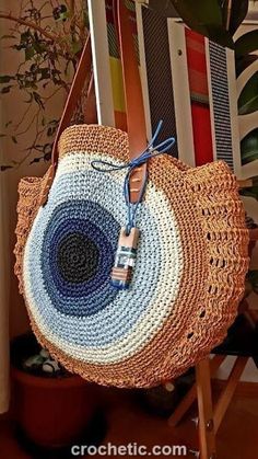 a straw bag with a blue and white design on it sitting on a chair next to a potted plant