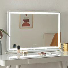 a white vanity with a lighted mirror on top of it and a vase filled with flowers