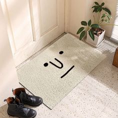 a pair of shoes sitting on the floor next to a door mat with a smiley face drawn on it