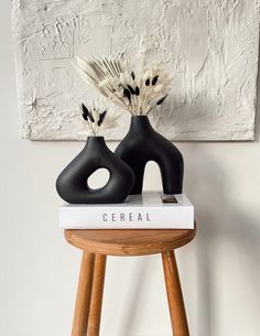 two black vases sitting on top of a white book next to a wooden stool