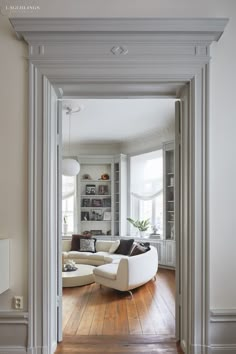 an open door leading to a living room with white furniture and bookshelves on the wall