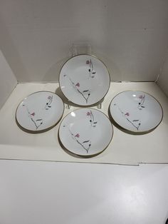 four white and gold plates with pink flowers on them in a display case for sale