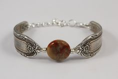 a silver bracelet with a red stone bead on the clasp and an ornate design