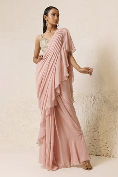 Dusty pink pre-draped ruffle saree with pearl embellishment edging. Paired with rhinestone embellished padded blouse.
Components: 2
Pattern: Blouse: Embellished
Type Of Work: Rhinestone
Neckline: Deep V Neck
Sleeve Type: Sleeveless
Fabric: Silk Georgette: Saree, Silk Crepe: Blouse 
Color: Pink
Other Details: 
Padded blouse
Attached inner lining
Length: (in inches)
Saree: 44
Blouse: 14
Pleat detail pallu
Occasion: Sangeet - Aza Fashions Pre-draped Georgette Dress With Ruffles, Traditional Draped Skirt For Wedding, Pink Draped Wedding Dress, Chiffon Saree With Ruffles In Traditional Drape, Wedding Saree With Ruffles And Draped Style, Ruffled Chiffon Saree In Traditional Drape, Wedding Saree With Draped Ruffles, Georgette Ruffle Dress With Traditional Drape, Traditional Drape Georgette Dress With Ruffles