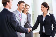 three business people shaking hands in front of a man and woman, both wearing suits