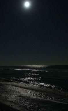 the moon is shining over the ocean on a dark night with no one in it