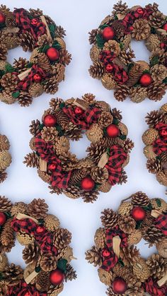 four wreaths made out of pine cones and red balls are arranged on a white surface