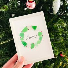 someone is holding up a card with the word love in front of a christmas tree